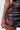 A close-up photo of a person wearing the BACK IT UP MINI SKIRT by AKIRA Label, which is a black faux leather mini skirt featuring pink and white flower embroidery along the side and red stitching at the hem. The individual is also sporting a black crop top, with a plain, light-colored background.