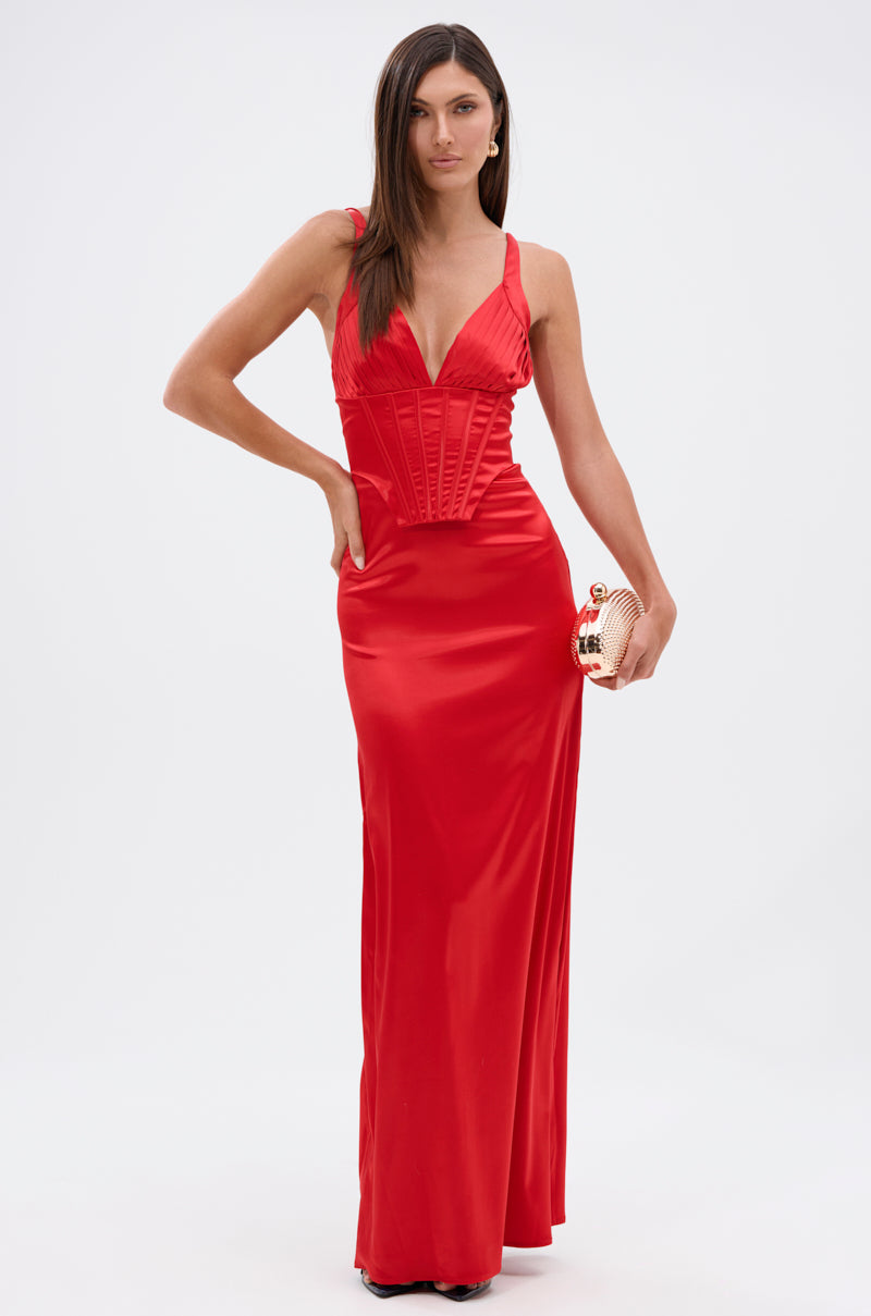 A woman in the ALL ABOUT ME SATIN MAXI DRESS with a plunging neckline and structured bodice holds a gold clutch, standing against a plain white background.