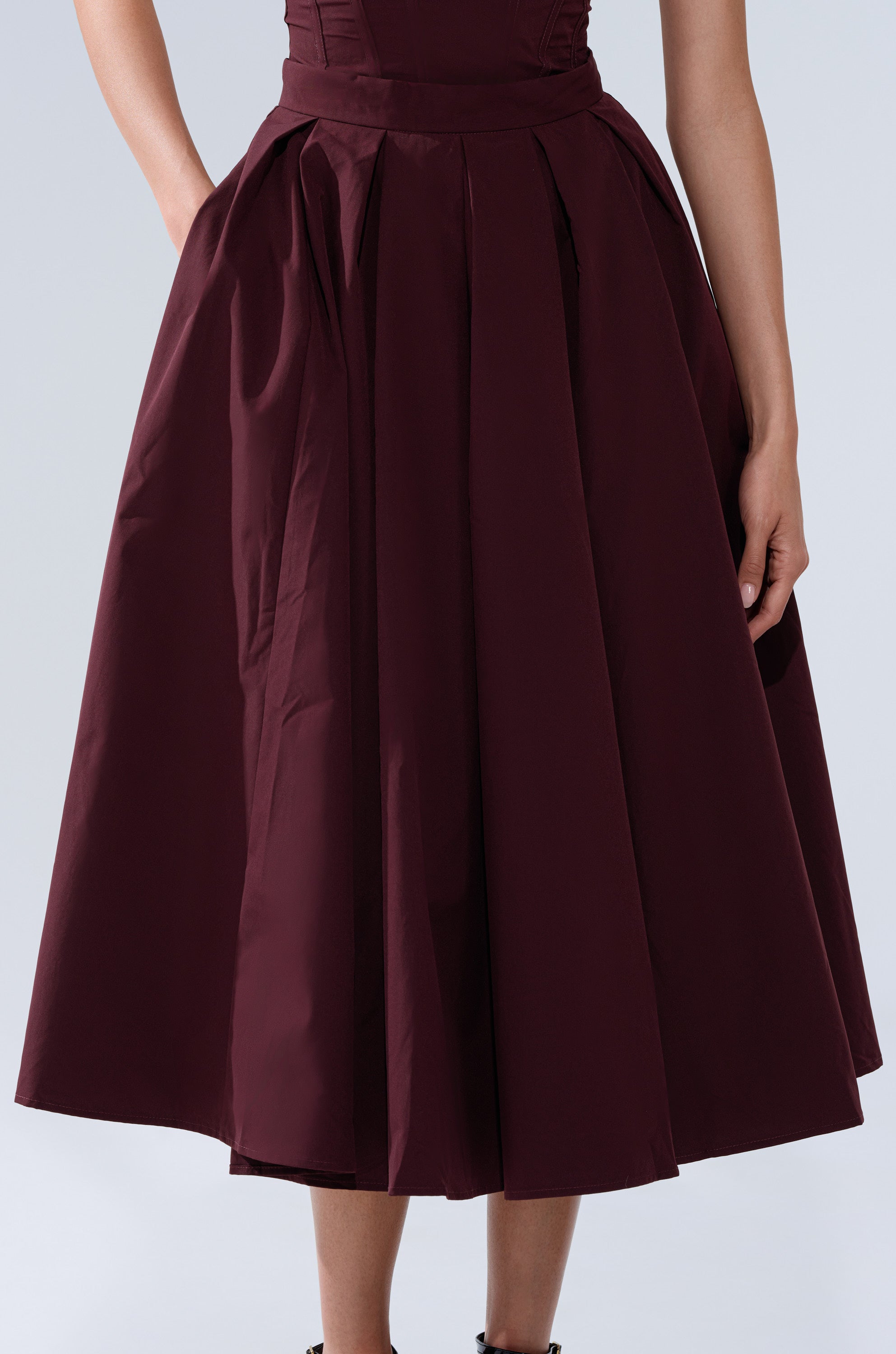 A person models the LOVE THIS FOR YOU MAXI SKIRT IN BROWN, a high-rise, pleated maxi skirt, with hands in pockets and photographed from shoulders to mid-calf against a light background. 8
