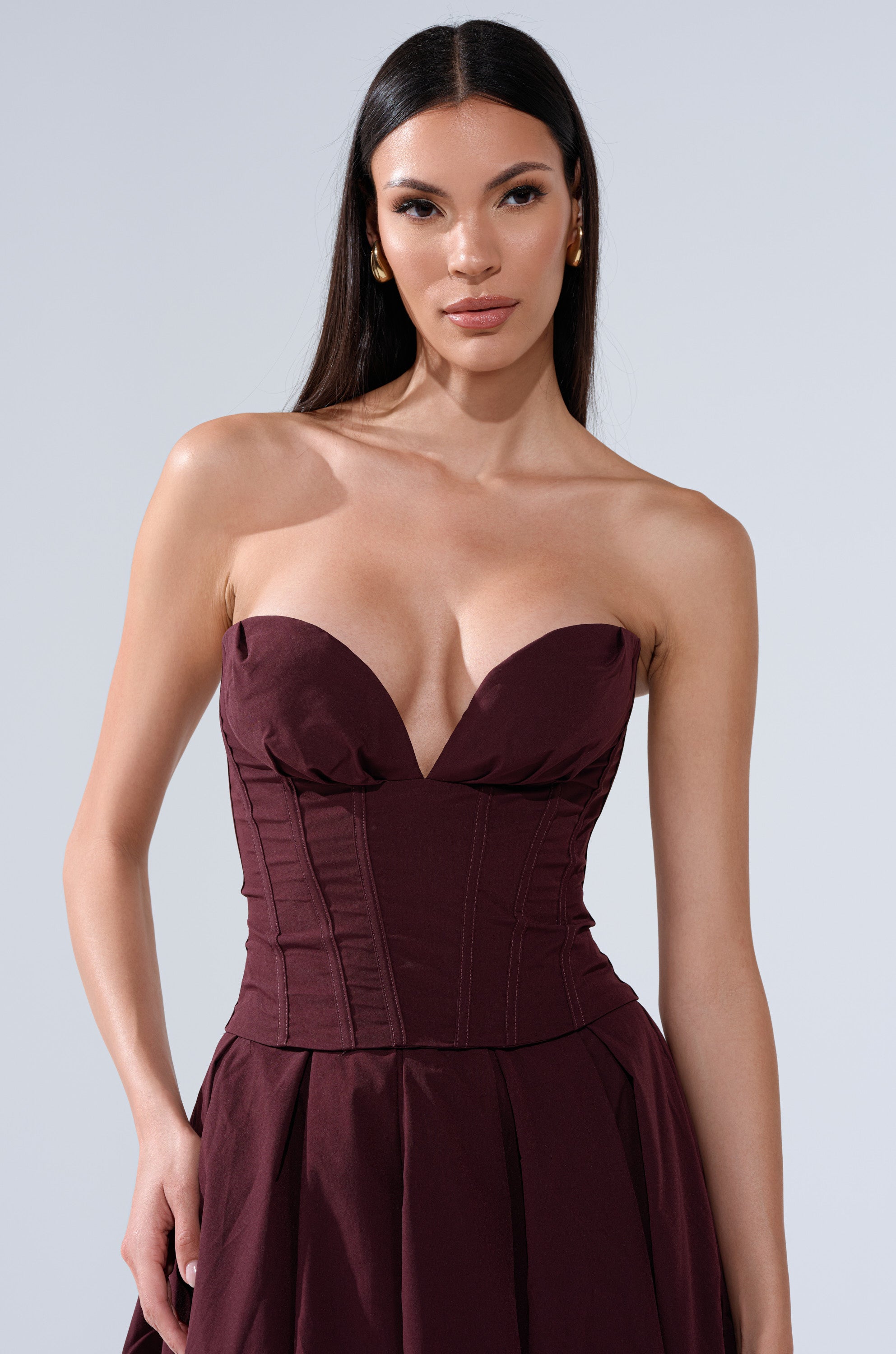 A woman with long, straight dark hair wears the LOVE THIS FOR YOU CORSET IN BROWN with a fitted bodice and flared skirt. She stands against a plain light grey background, looking confidently at the camera. 1
