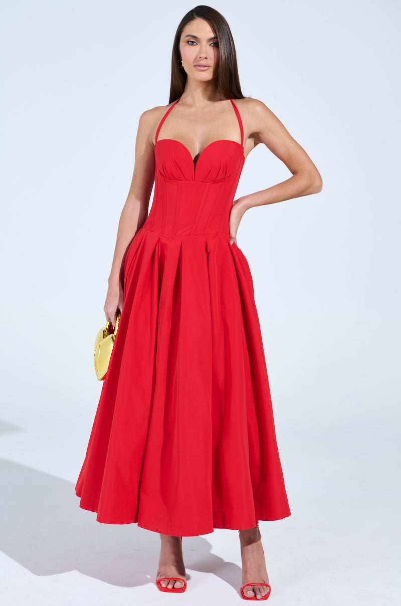 Wearing a striking red, strapless DOLCE DREAMING MIDI DRESS WITH CORSET, a person poses against a plain background, gracefully holding a small round yellow bag and sporting chic red open-toe shoes. Their long, straight hair perfectly complements the ensemble.