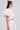 A woman with long brown hair in a half-up style wears the cream satin GIRL POWER CROP TIE FRONT TOP with a matching high-waisted skirt and statement earrings, posing in profile against a plain background.