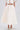 A person wears the off-white GIRL POWER MIDI SKIRT with an A-line, high-waisted ankle-length design and a matching short-sleeved cropped top with front tie, paired with embellished high-heeled shoes. Face is not shown.