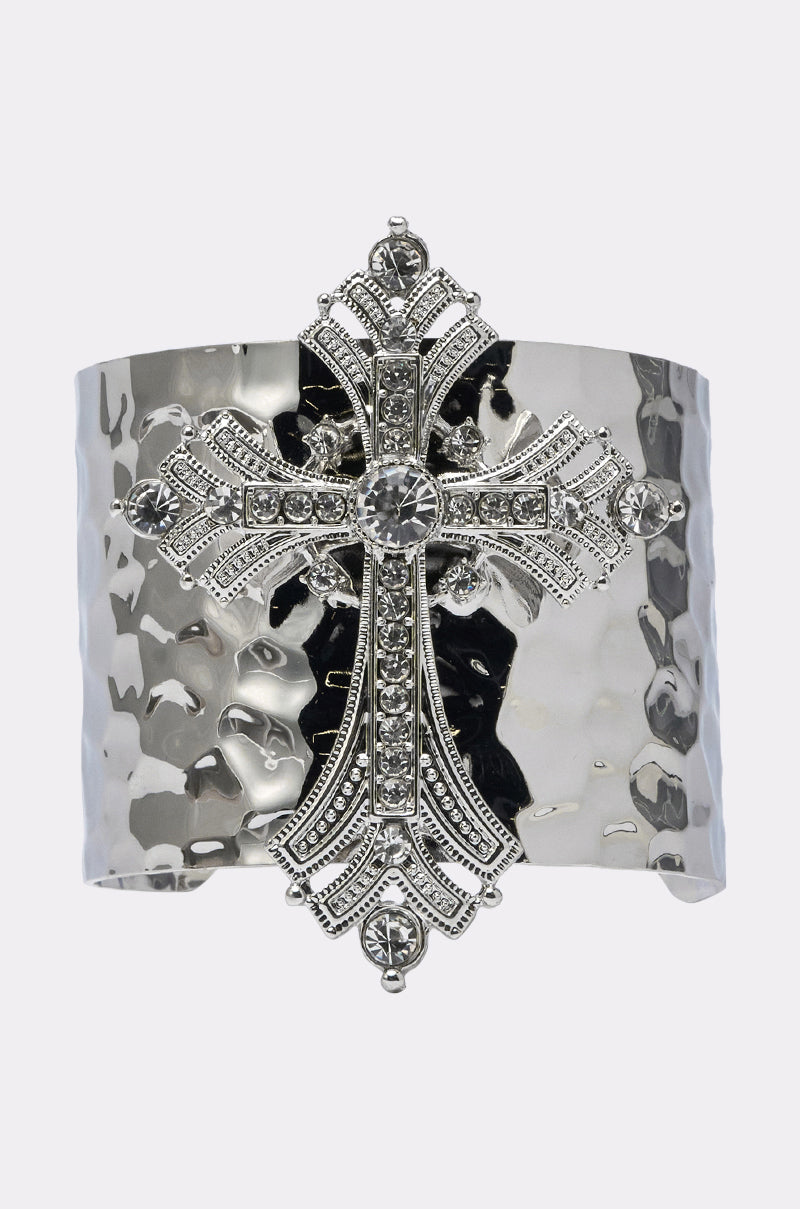 The GIVING ENERGY CUFF is a wide hammered silver bracelet with an ornate cross pendant at the center, accented by sparkling rhinestones. 0