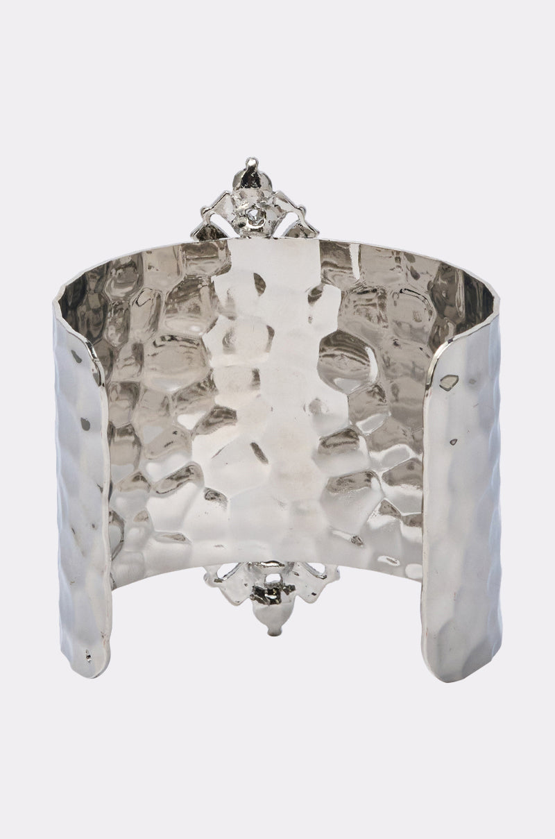 The GIVING ENERGY CUFF is a wide, hammered silver cuff bracelet with an open back and ornate center detailing. Its textured, reflective finish features subtle rhinestone accents, displayed against a plain light-colored background. 3