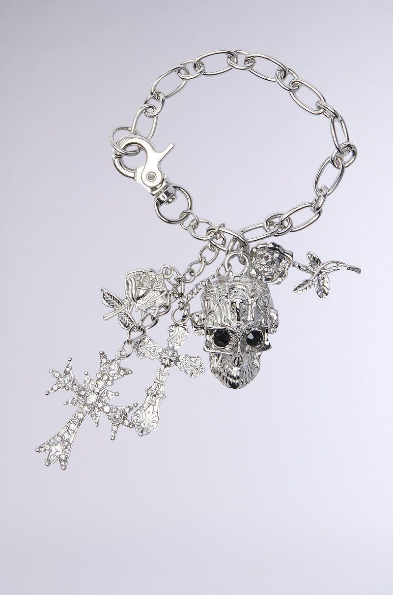 The FOREVER BLESSED BRACELET features large Cuban links, intricate charms including a rhinestone-eyed skull, detailed angel, floral-patterned cross charms, a rose, and a small wing—all set against a light gray background.
