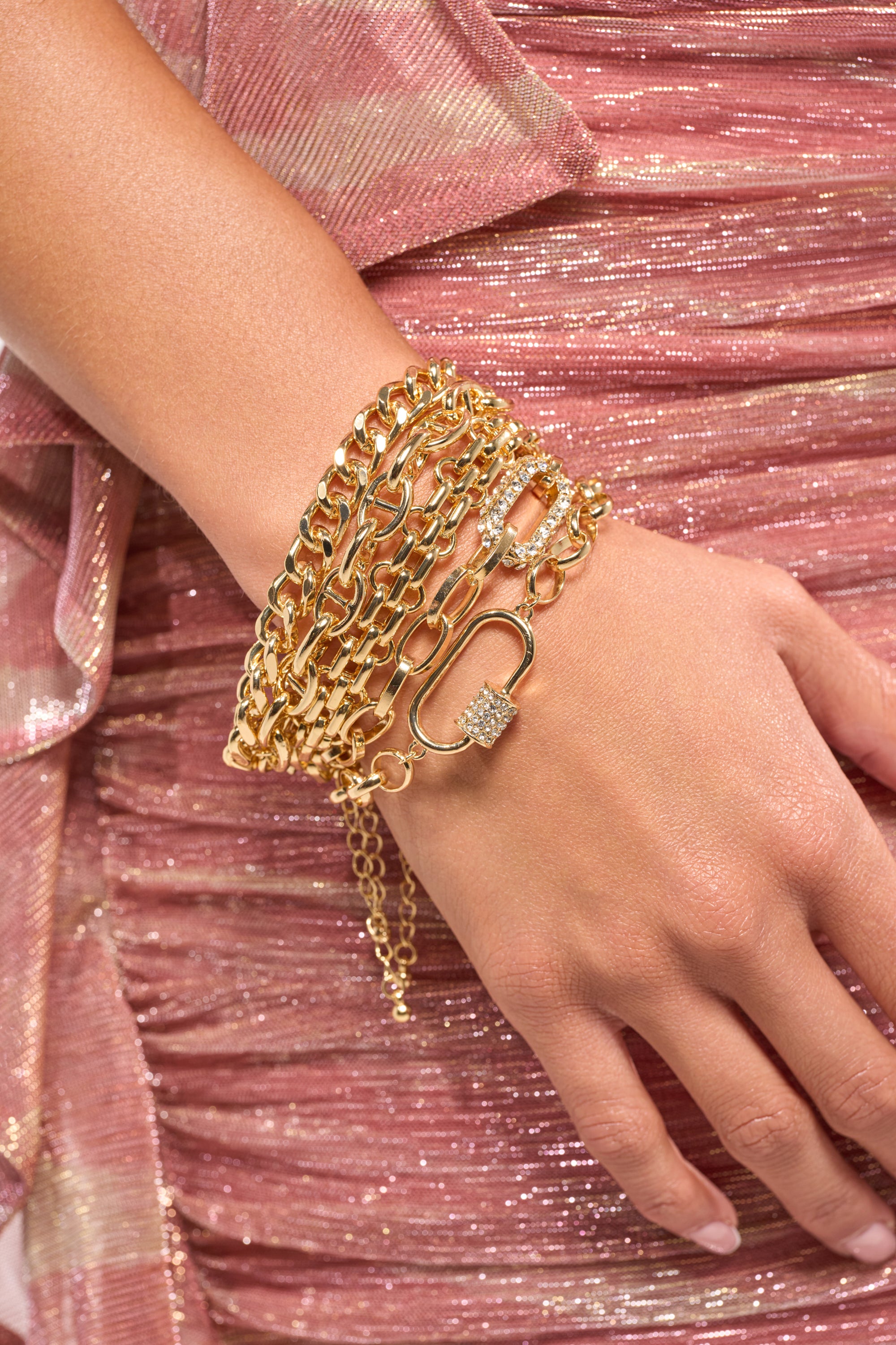 A woman wears the REGAL BRACELET SET IN GOLD on her wrist, paired with a shimmery pink ruched fabric dress. Her relaxed hand at her side accentuates both the jewelry and the textured dress.