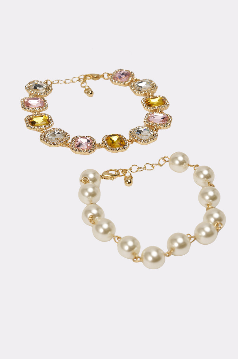 The REGENCY BRACELET SET features a vibrant gemstone tennis bracelet with colorful stones in gold settings and an adjustable faux pearl bracelet with round white pearls and gold accents, displayed elegantly on a plain white background. 3
