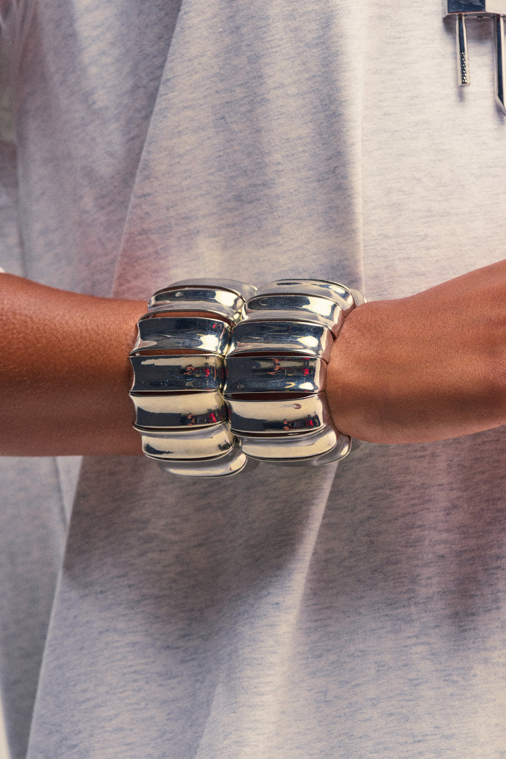 A person wearing a light gray shirt with the ULTIMATE CUFF SET—two large, chunky silver bracelets on their wrist showcasing a segmented, ridged design reminiscent of wide ribbed cuffs.