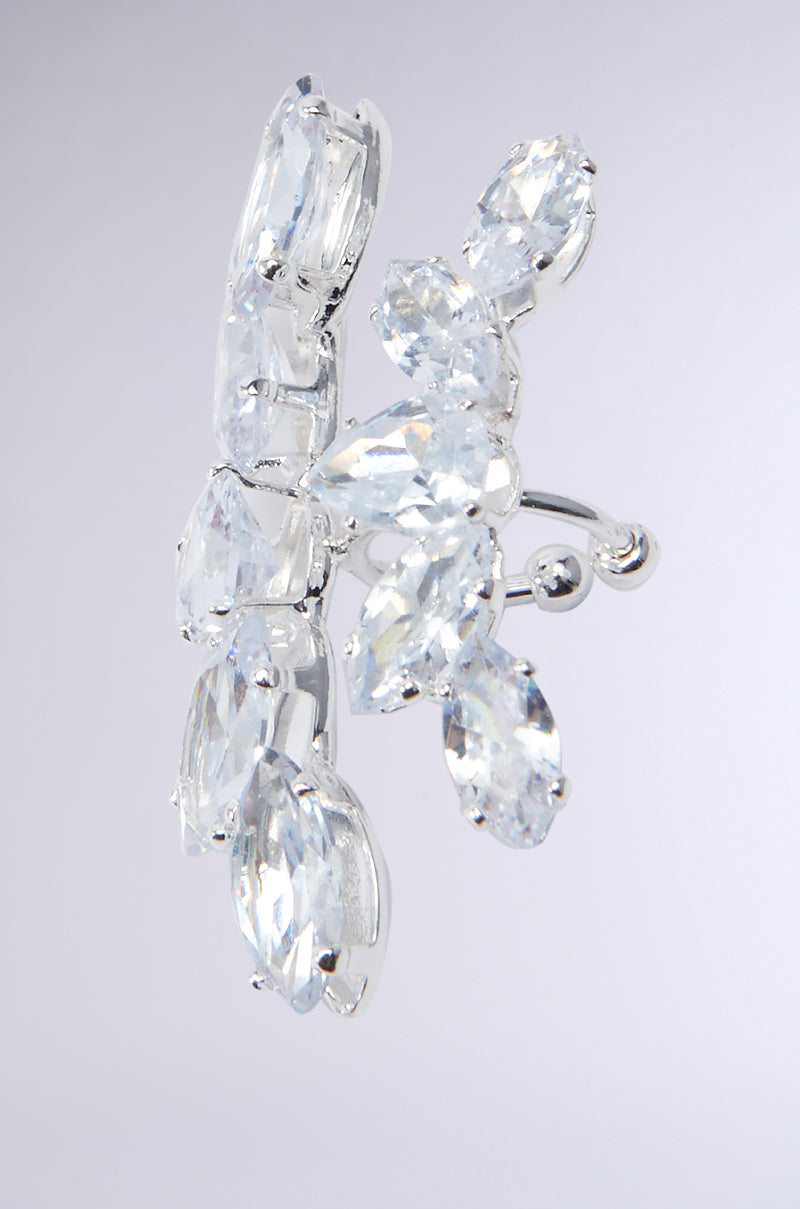 A close-up of a silver ear cuff adorned with clear, marquise-cut crystals showcases a floral design, with crystal petals elegantly surrounding the central piece, reflecting the sophistication found in the CHARMER FAUX LIP RING by AKIRA. 3