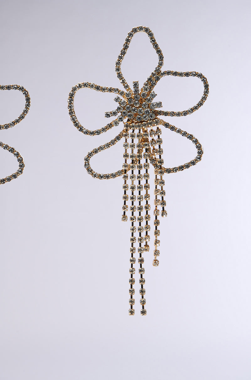 The IN THE GARDEN EARRING sparkles on a gray background with ornate, rhinestone-encrusted floral silhouettes. Central clusters radiate chain-like strands in a cascading style, perfect as statement earrings for any elegant occasion.