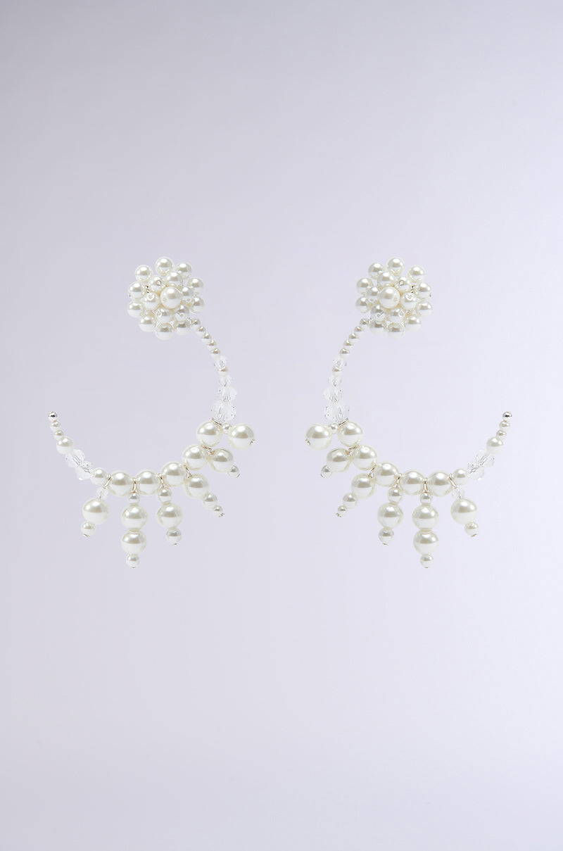 The I AM A RICH MAN EARRING from the AKIRA Label features an elegant floral design at the top, with curve-shaped strands adorned with smaller dangling pearls. The soft, light gray background accentuates the delicate structure of these exquisite accessories.