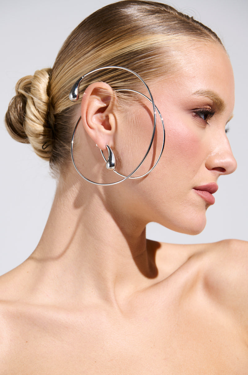 Profile of a person with blonde hair in a sleek bun, adorned with the artistic WRAP ME AROUND EAR CUFF. The skin looks smooth and the makeup is subtle, focusing on highlights and contouring, against a simple light gray background.