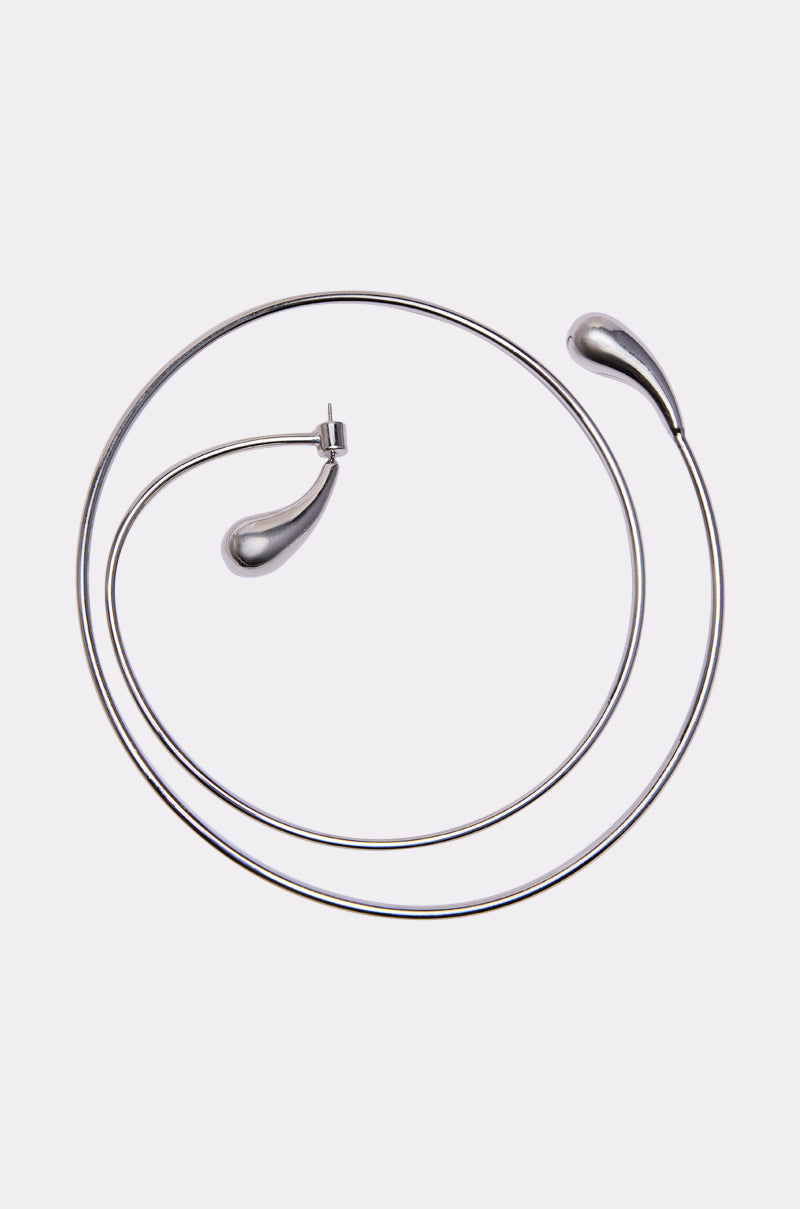 The WRAP ME AROUND EAR CUFF is a minimalist silver accessory with a thin, circular wire design and teardrop-shaped ends, shown on a plain white background.