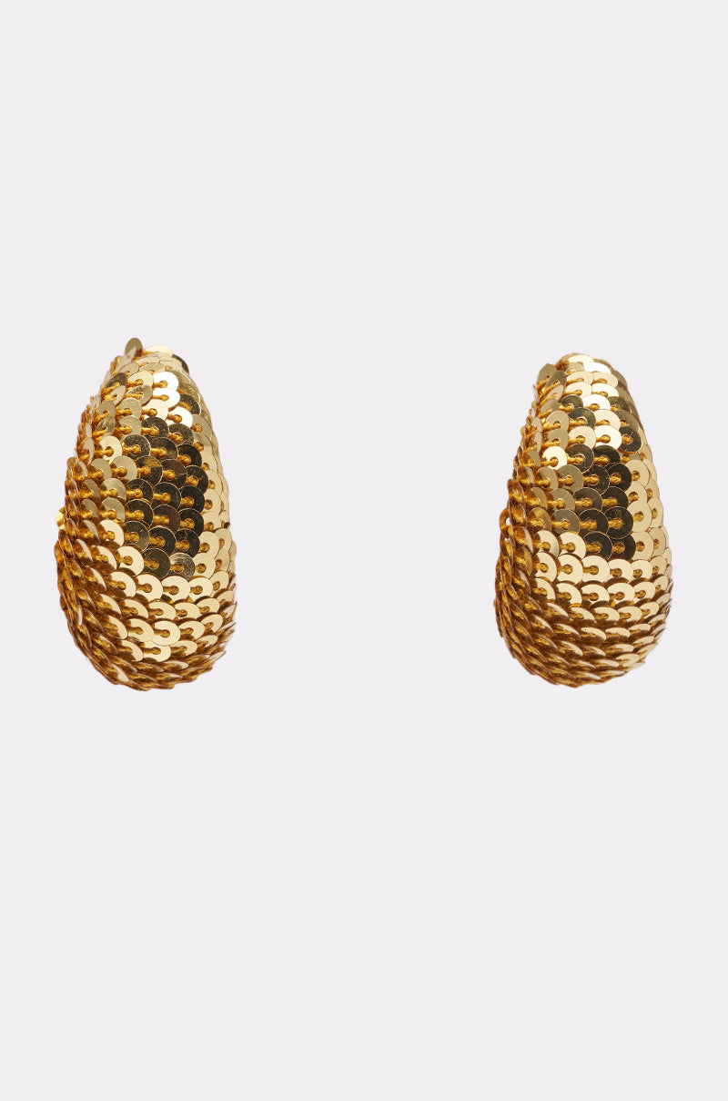 The GIMME THE GLITTER HOOP EARRING features teardrop-shaped, disco-glam hoops covered in shiny gold sequins, displayed against a plain white background. 3