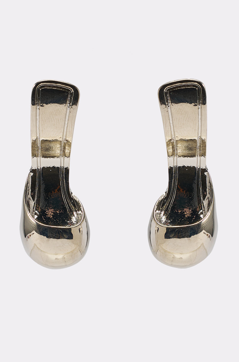The WALK IN MY SHOES EARRING is a pair of shiny, silver-tone stud earrings with a curved, sculptural, abstract design, shown against a plain light gray background. 2