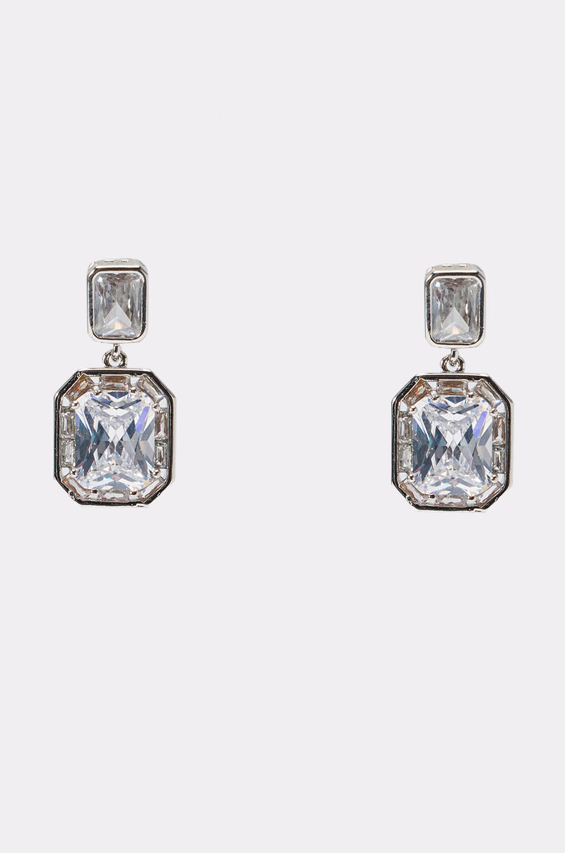 The DIAMONDS ARE MY LOVE LANGUAGE EARRING features silver drop earrings with a small square-cut clear gemstone atop a larger rectangular crystal, creating a bold statement look against a plain white background.