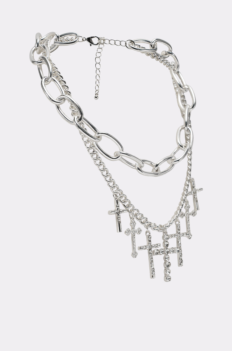 The CROSS MY HEART SILVER NECKLACE is a layered silver chain with chunky oval links, a medium strand, and a third layer adorned with sparkling rhinestone-studded cross pendants. 3