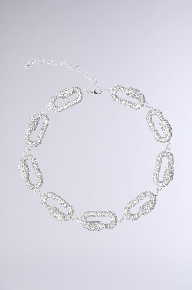The TESSA NECKLACE is a stunning silver piece with interconnected oval-shaped links, each adorned with sparkling rhinestones arranged in a circular pattern. It features an adjustable closure to ensure the perfect fit against a plain, light gray background.