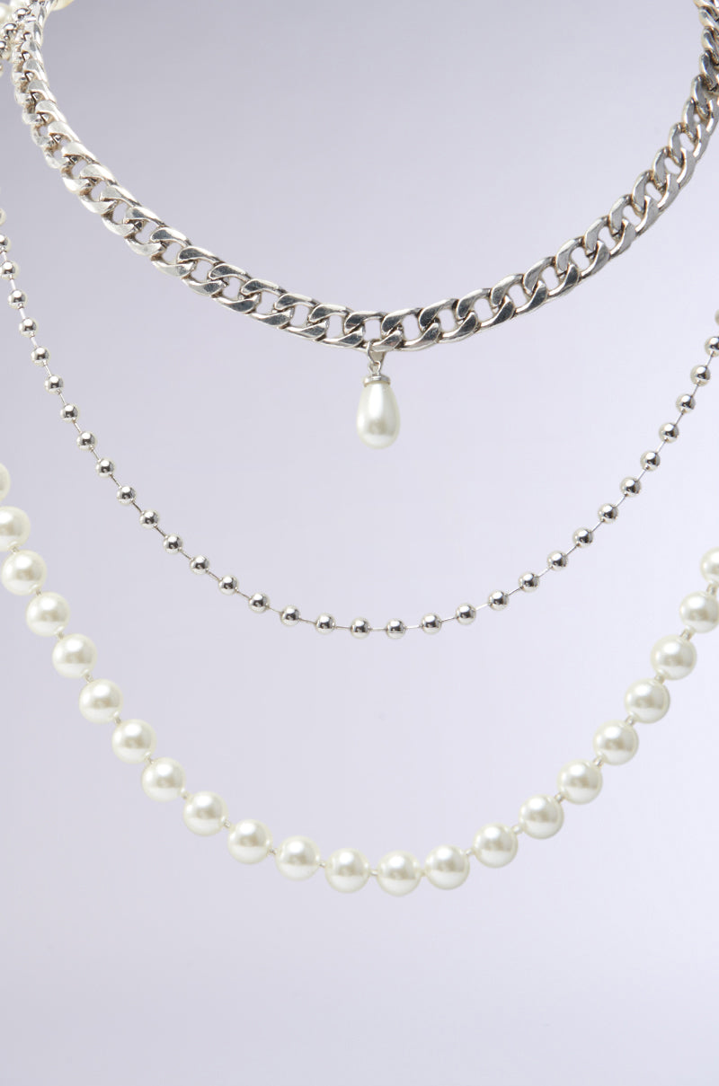 The GLAM LIFE LAYERED NECKLACE set displays elegantly against a light gray background, featuring a faux silver chain with a pearl pendant, a delicate silver chain, and a string of white pearls, all arranged in a cascading style. 2
