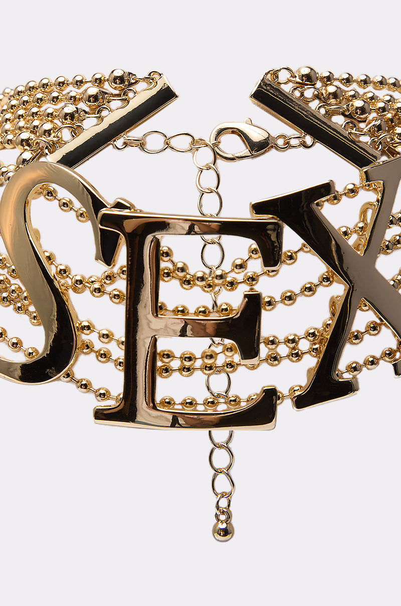 Make a statement with the LETS DO IT NECKLACE—a bold gold-tone choker featuring layered chains and large metallic letters spelling "LETS DO IT" across the front.