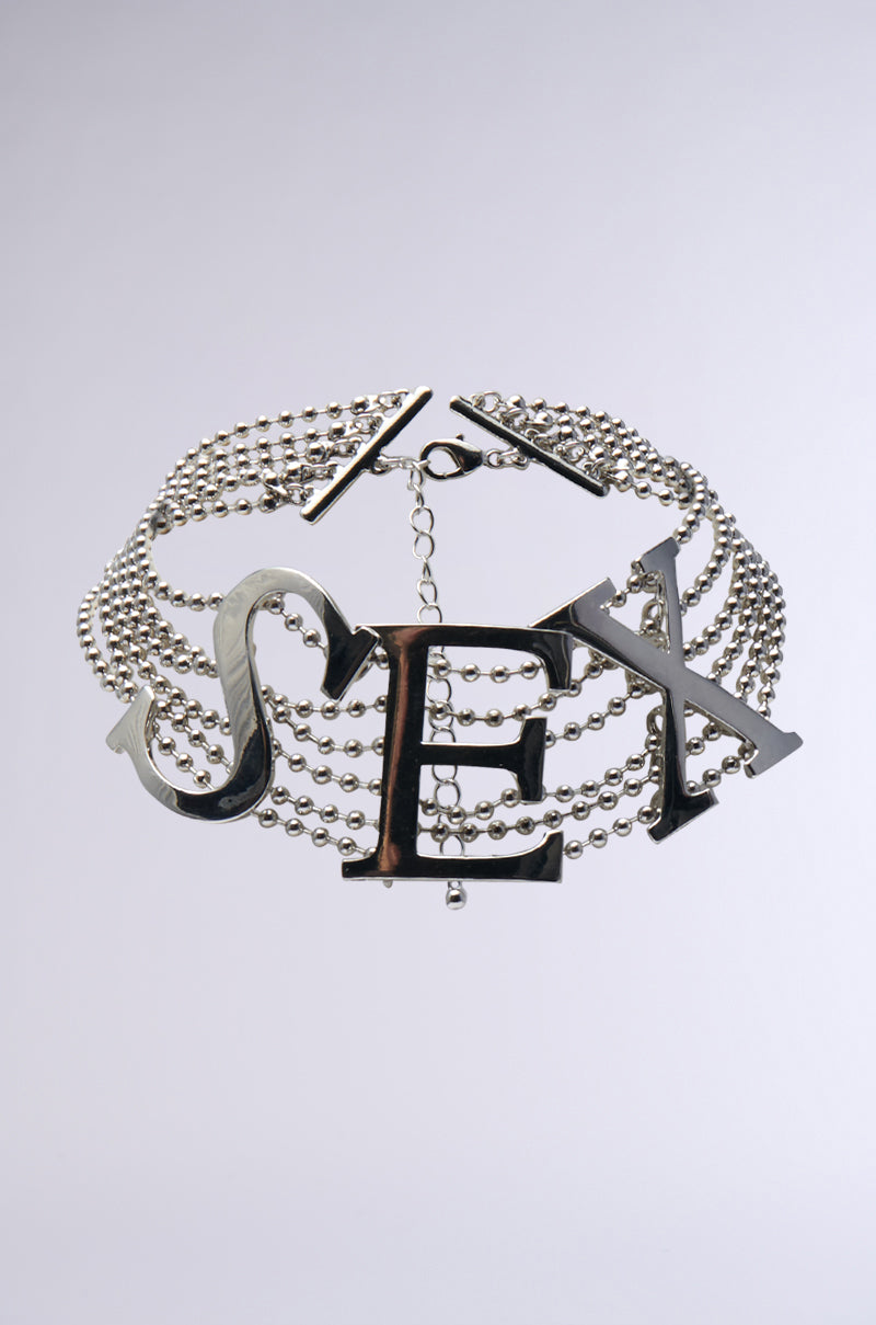 The TOO SEXY CHOKER is a dazzling faux silver necklace featuring multiple strands of small beads, accented by large metallic letters spelling "SEX" at the center. It includes an adjustable lobster clasp to ensure a perfect fit.