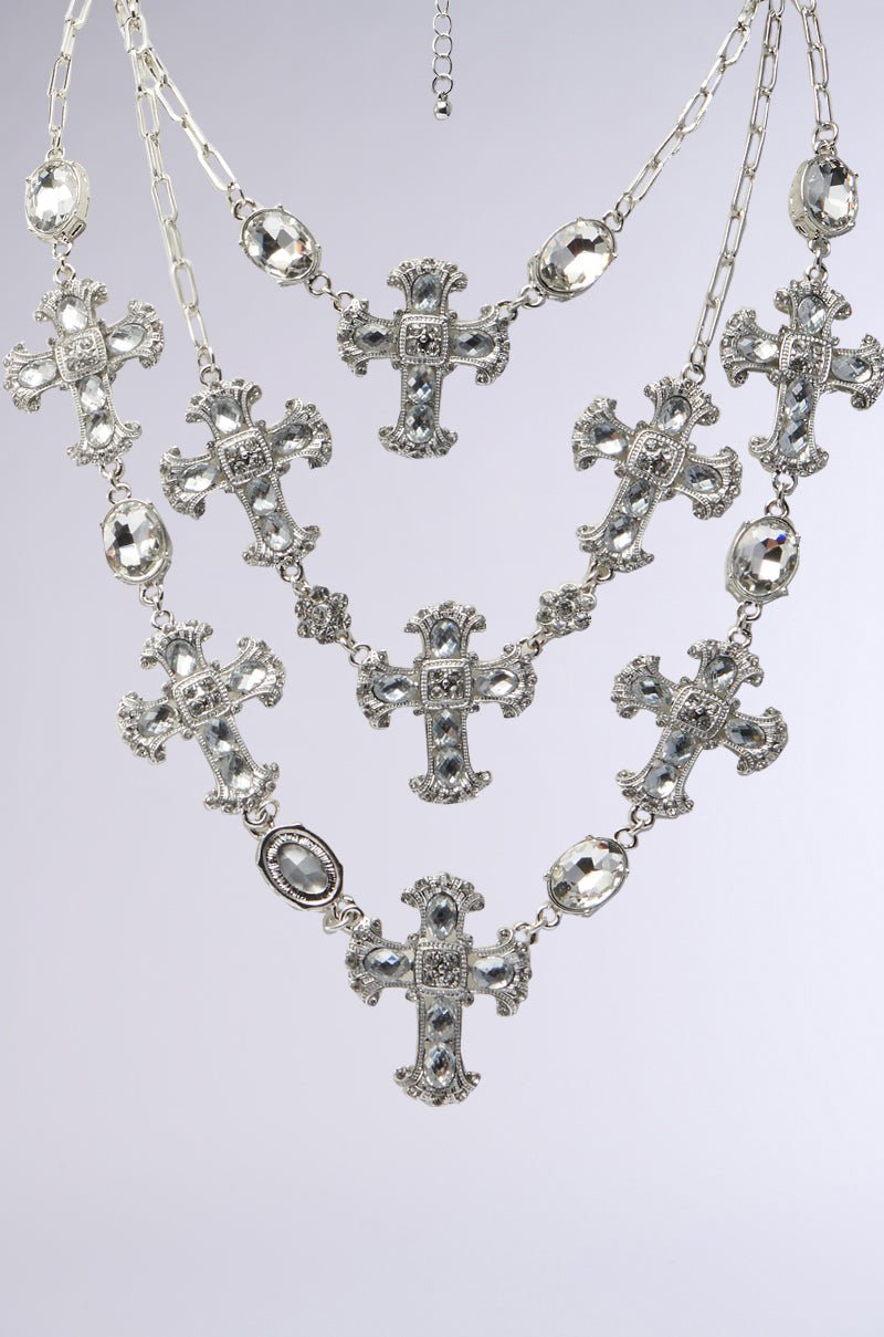 The SO TRENDY NECKLACE is a stunning piece with triple-layer chain links and rhinestone cross charms, adorned with gemstone-studded pendants and large oval jewels, creating an elegant look on a light gray background. 5