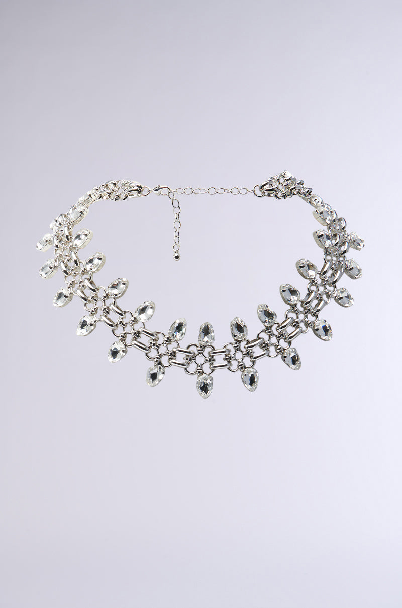 THE REAL WILL KNOW NECKLACE is a delicate faux silver choker adorned with multiple clear, teardrop-shaped crystals arranged symmetrically. It features an adjustable chain clasp and is presented against a plain, light gray background. 0