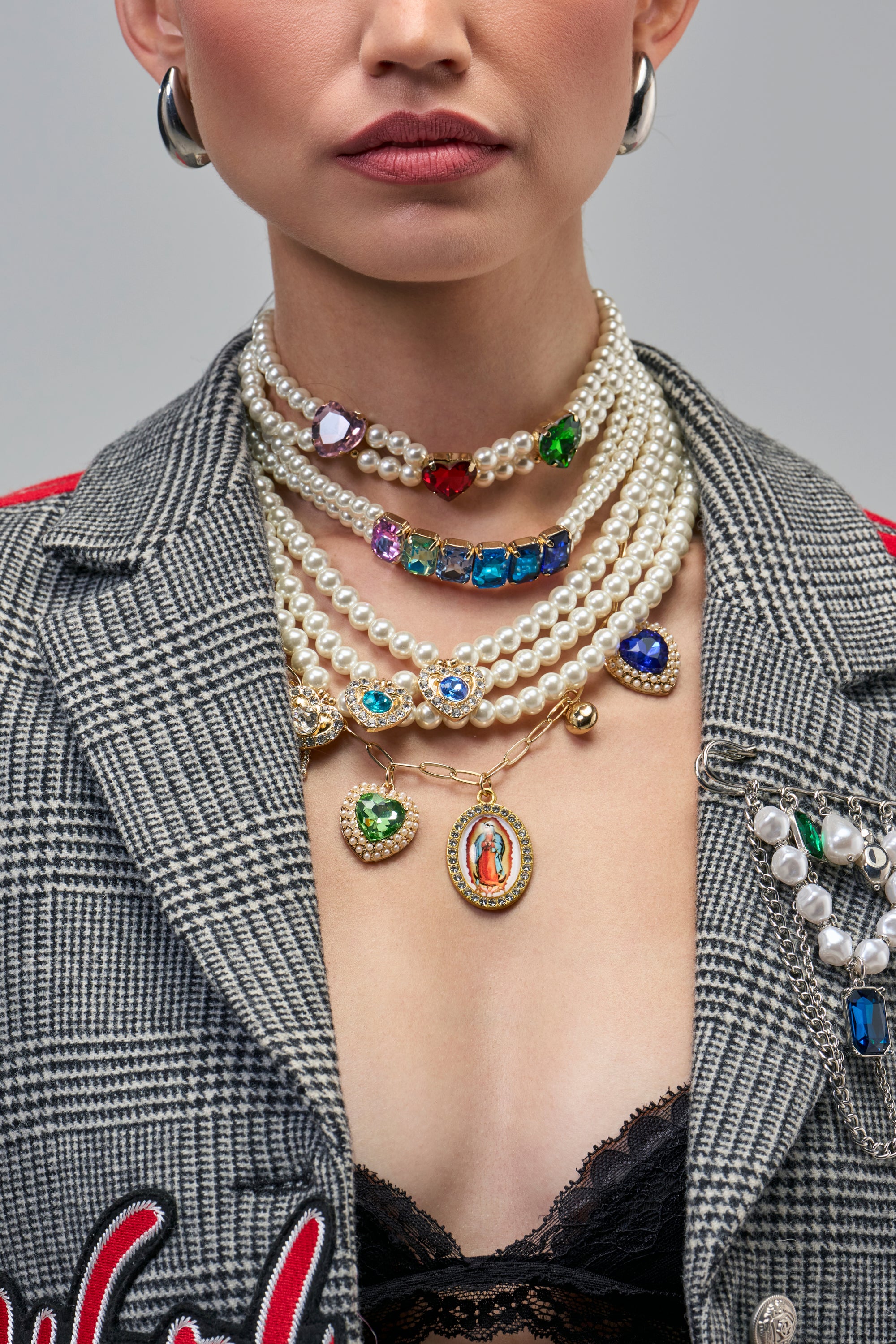 Model wearing the FEEL MY VIBE NECKLACE, featuring layered multiple pearl strands with colorful gemstone accents and a central oval pendant depicting a religious figure.
