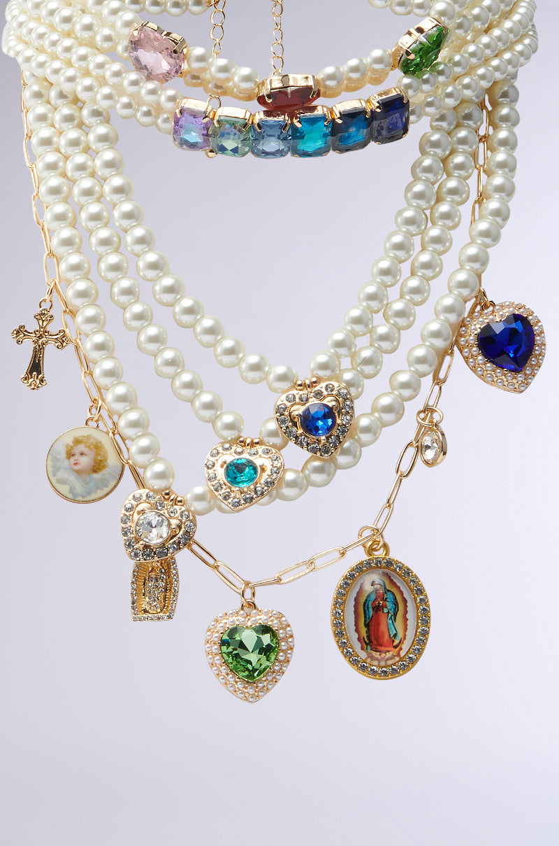 The FEEL MY VIBE NECKLACE collection features ornate choker necklaces combining pearl strands and gold chains, embellished with heart-shaped gemstone pendants, a child's photo, a religious pendant, and a crucifix charm against a light backdrop.