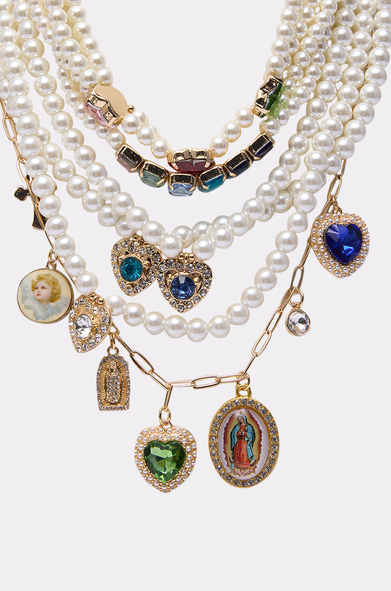 The FEEL MY VIBE NECKLACE is a layered set with pearl strands, colorful crystal beads, gold chains, and charms like hearts, lockets, rhinestones, an angel, and a religious icon. 2