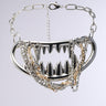 The BITE ME NECKLACE is a bold piece with large metallic spikes in a zigzag pattern, interspersed with faux silver chains and rhinestones, mimicking jagged teeth on a linked chain.