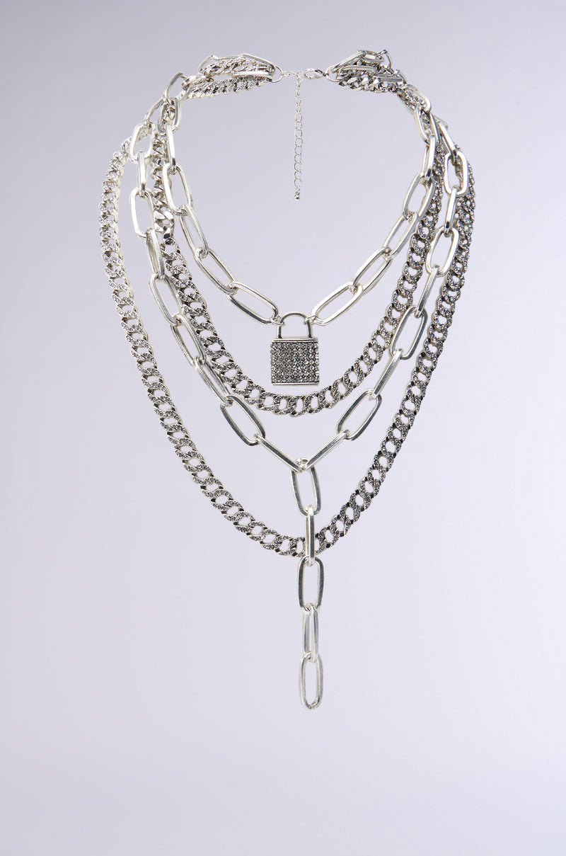Introducing the FEEL MY ENERGY LOCK LAYER NECKLACE by AKIRA Label, featuring a large rhinestone padlock charm. This statement piece combines various chain styles with both chunky and intricate links to create a bold and stylish accessory.