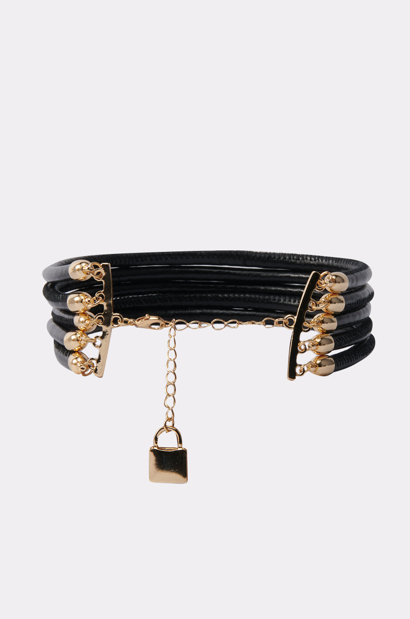 The KEY TO MY HEART NECKLACE features black multi-strand cords, gold-tone hardware, decorative gold beads, and a small gold padlock charm—perfect for adding edgy elegance to any look.