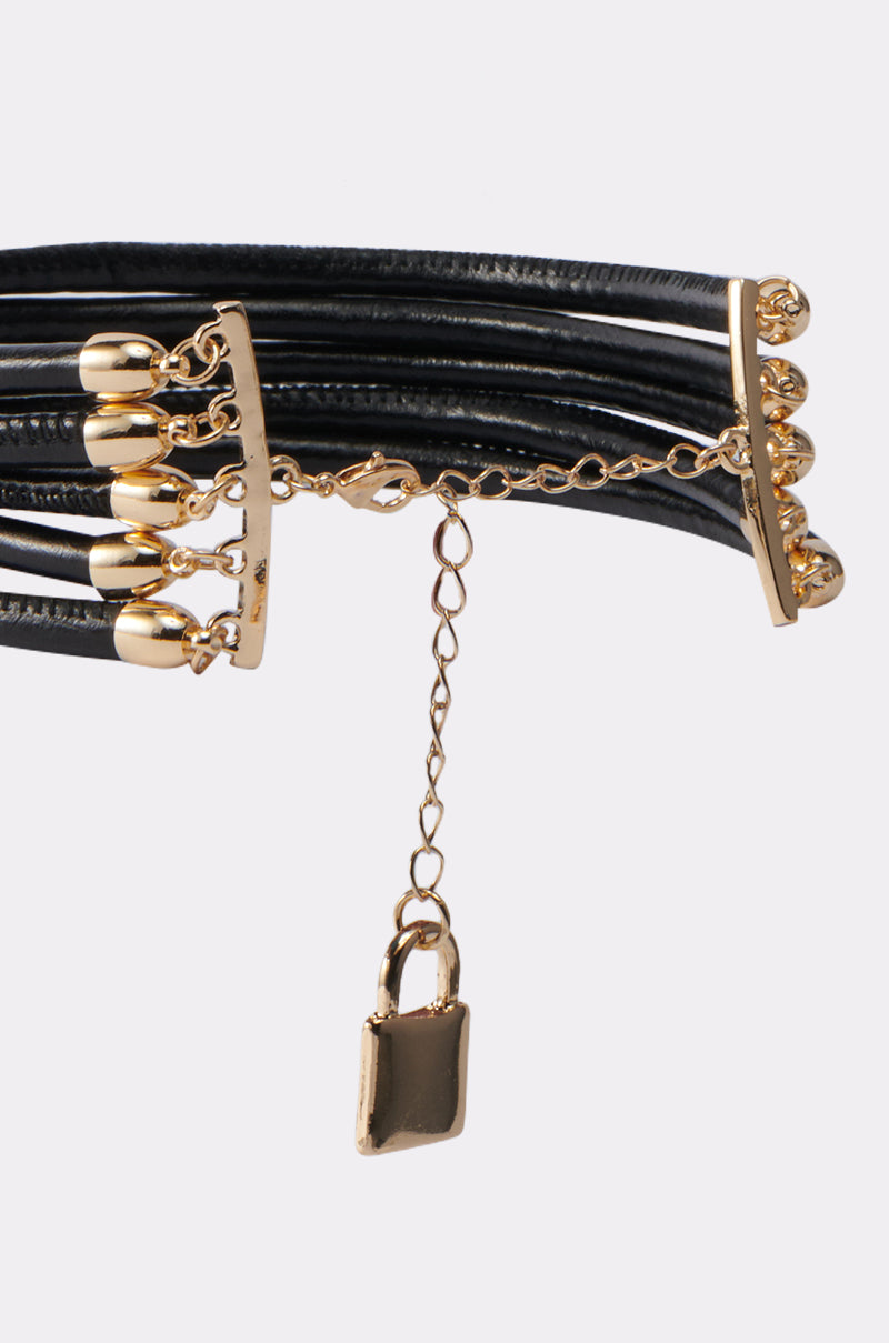 The KEY TO MY HEART NECKLACE is a black multi-strand choker with gold hardware, featuring a gold chain and a small gold padlock charm at the center for a chic, romantic touch.