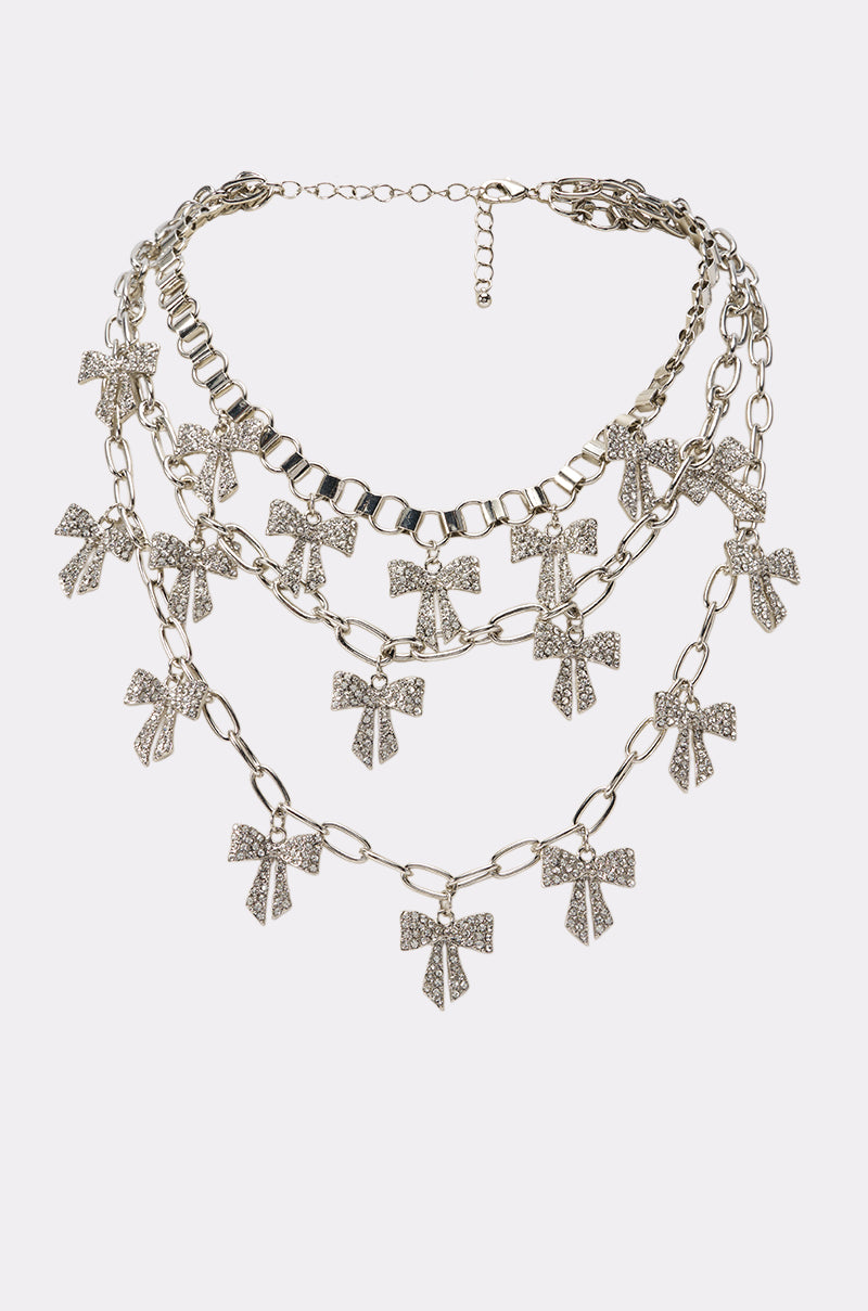 Introducing the TIED IN A BOW NECKLACE: a stunning layered silver necklace featuring multiple sparkling rhinestone-encrusted bow-shaped pendants, beautifully presented against a plain white background. Perfect as festival jewelry, this elegant piece adds a glamorous touch to any ensemble.