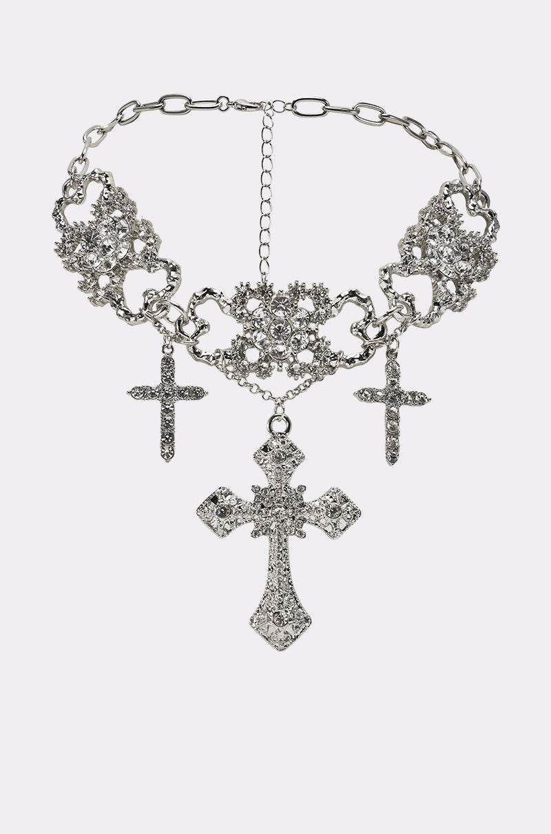 The FOREVER PROTECTED NECKLACE is a silver statement piece with ornate metalwork, three dangling jeweled crosses, and an adjustable chain clasp at the back. 0