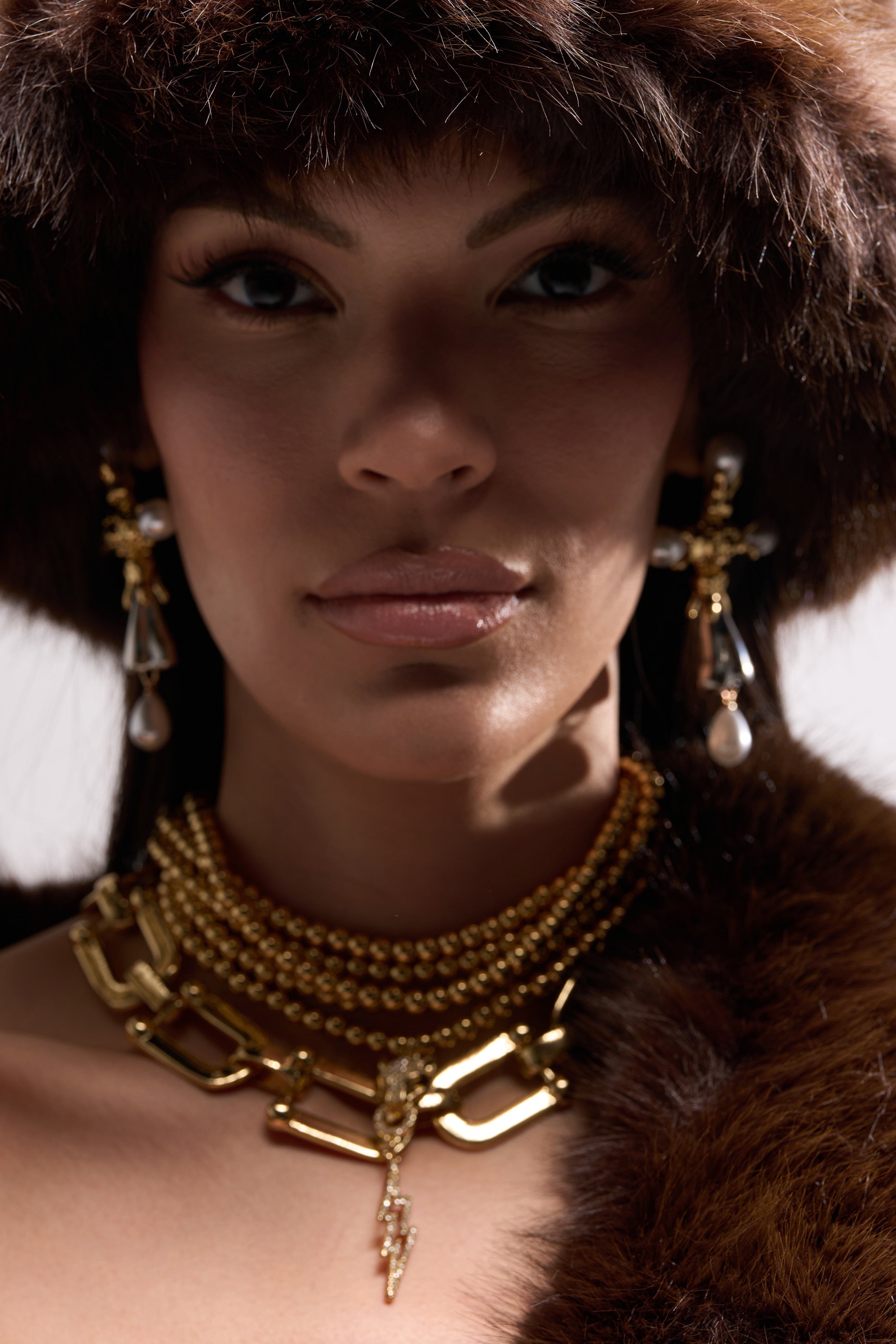 A woman in a large fur hat and matching garment models elegant gold jewelry, featuring the GOLD QUEEN NECKLACE SET with layered gold-tone chains and a bold panther head pendant, confidently gazing at the camera. 1