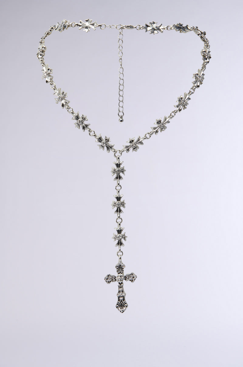 The DEDE CROSS NECKLACE is a silver rosary-style piece with star-shaped floral links featuring rhinestone centers and a decorative cross pendant. It is shown against a plain, light gray background.