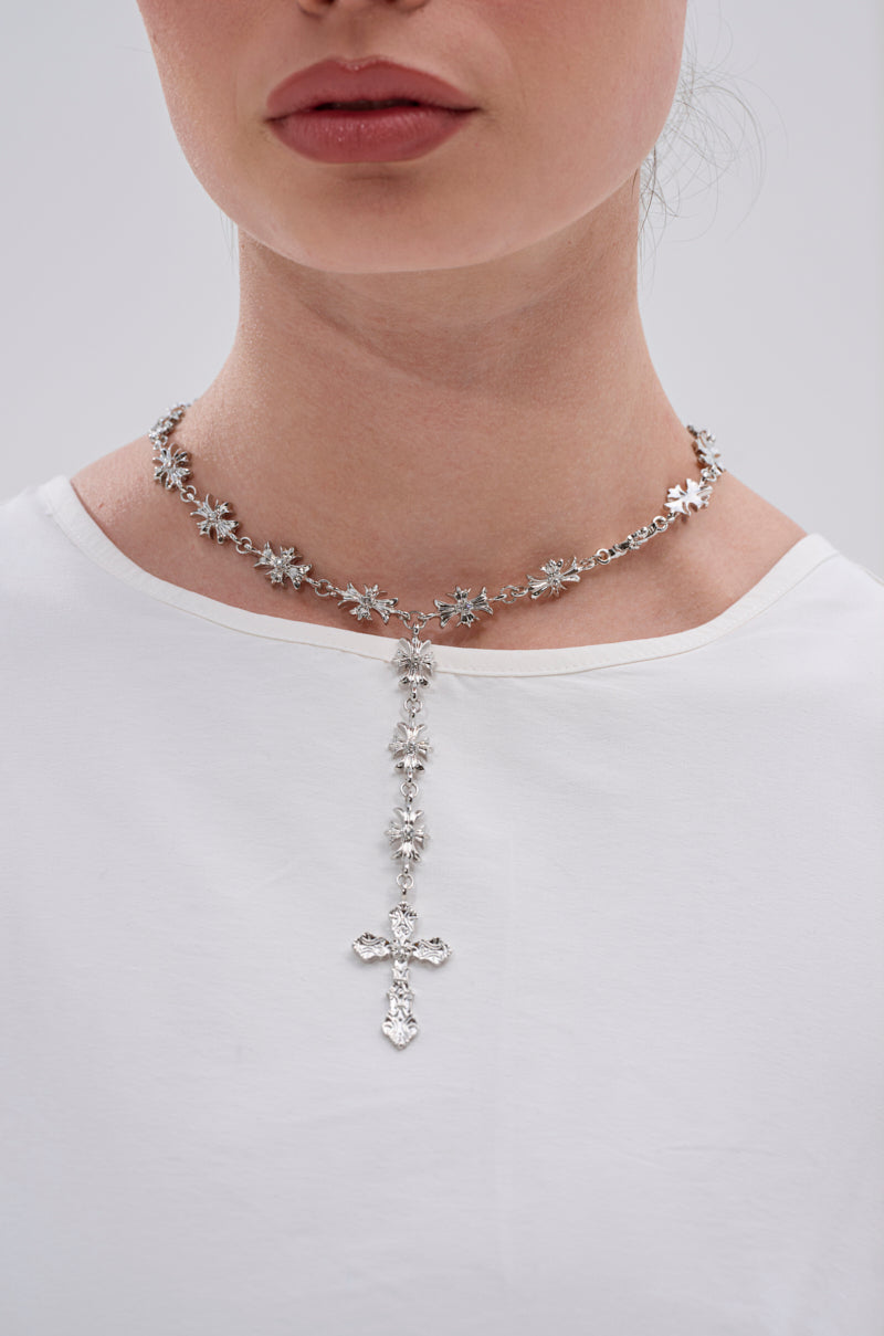 A woman wears a plain white top and the DEDE CROSS NECKLACE, featuring star-shaped links with rhinestone centers, photographed from the shoulders up against a light background.