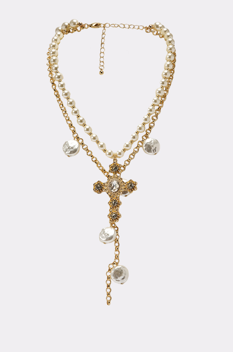 The JUST A LITTLE CHI NECKLACE features two gold pearl layers with crystal detailing, a large ornate rhinestone cross pendant, hanging pearl accents, and an adjustable clasp. 1