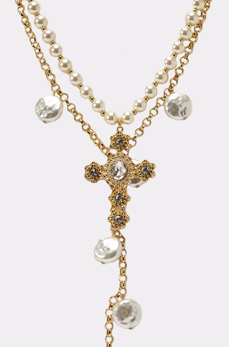 The JUST A LITTLE CHI NECKLACE is a layered piece featuring a gold chain with a gold cross pendant, crystal accents, and large pearl-like beads. 2
