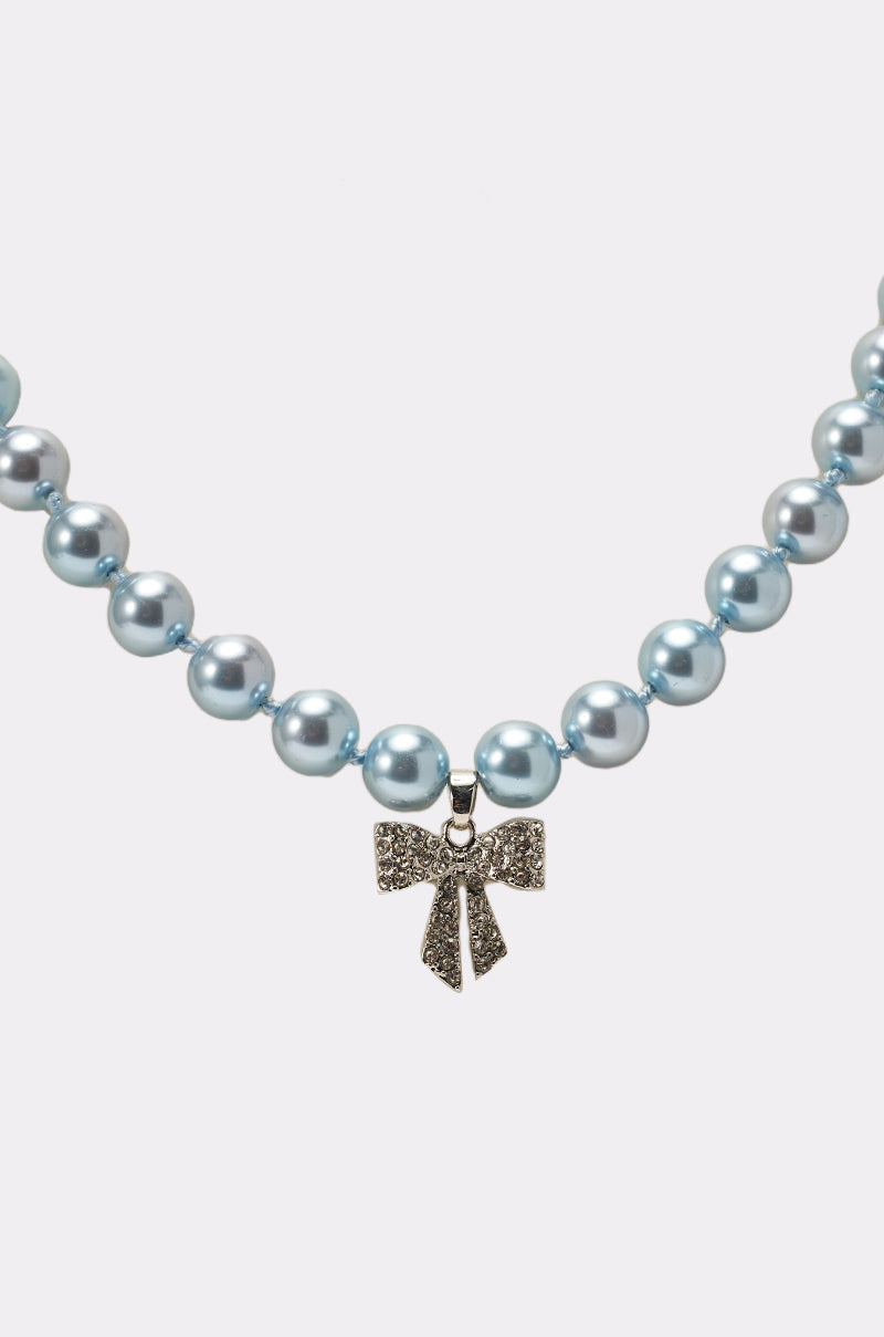 The KRISTEN NECKLACE is a blue pearl necklace with a central crystal bow pendant embellished with small crystals, shown on a plain white background. 2