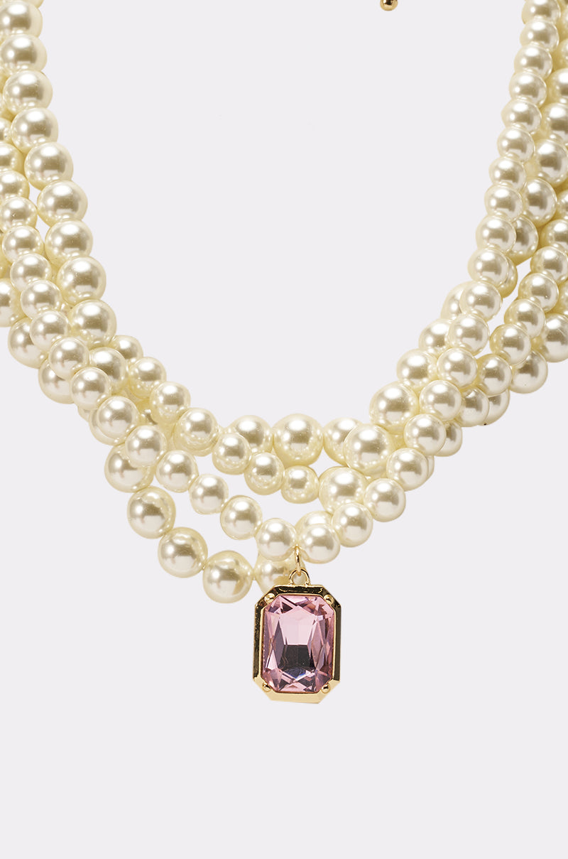 The MARIE LAYERED NECKLACE features faux pearls and a large rectangular pink gemstone pendant set in gold, shown on a plain white background. 2
