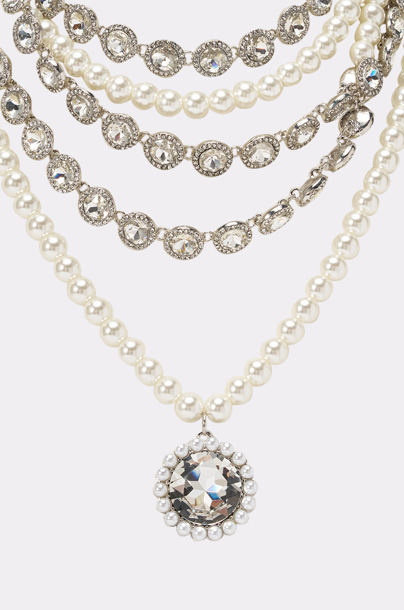 The ARI NECKLACE features five layers with alternating pearl and rhinestone strands; the lowest layer displays a crystal bib pendant adorned with pearls and a central faceted gem, making it perfect for formal jewelry looks. 2
