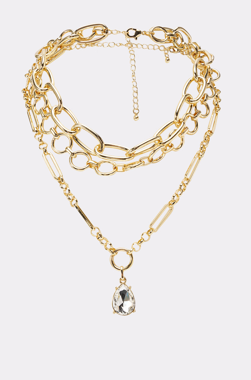 The REGENCY NECKLACE is a layered gold chain with mixed link styles and a teardrop clear crystal pendant on the shortest strand. This adjustable necklace features a user-friendly clasp for easy wear. 0