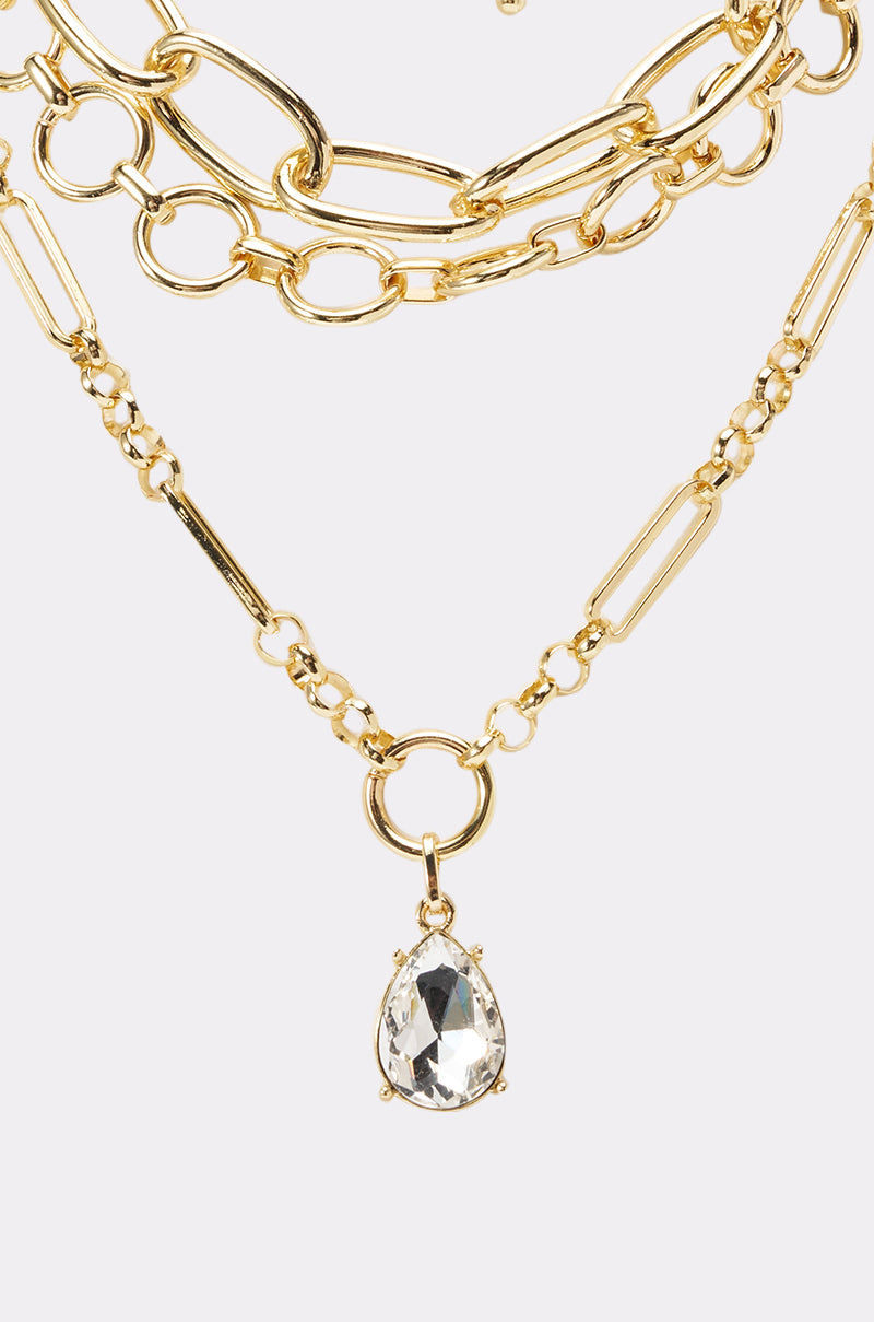The REGENCY NECKLACE features layered gold chains with mixed link styles and a clear teardrop crystal pendant—a stunning choice for maximalist jewelry lovers, shown against a light background. 2