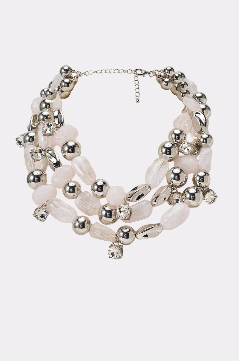 The ON VACA NECKLACE is a layered statement piece with three strands of large irregular pale pink beads, shiny silver beads, clear faceted crystals, sparkling crystal charms, and an adjustable clasp. 0