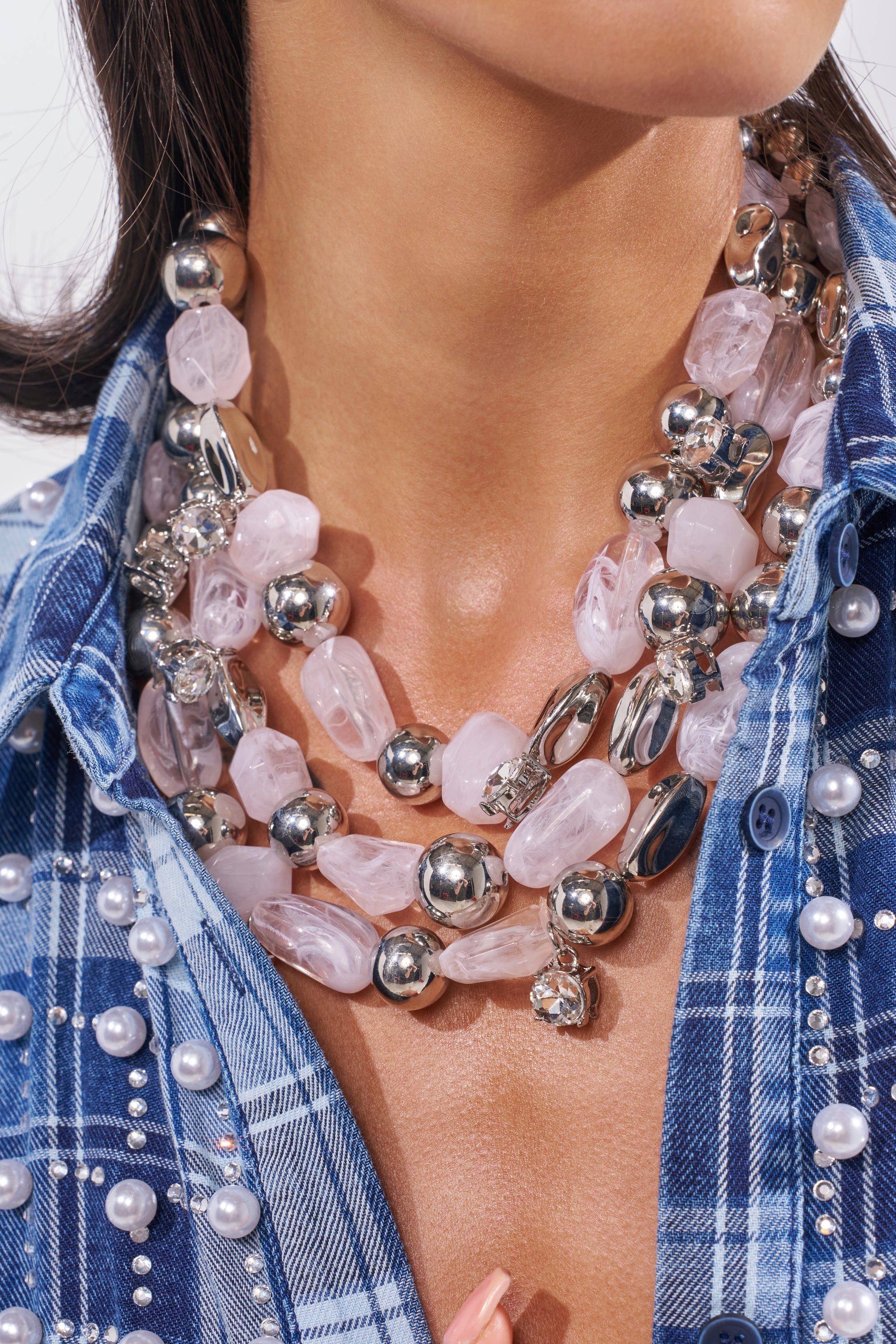 Wearing a blue plaid shirt with pearl details, the woman styles the ON VACA NECKLACE—chunky pink stones, silver beads, and crystal charms—layered elegantly around her neck. 1