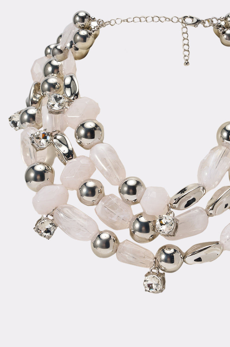 A close-up of the ON VACA NECKLACE, showcasing multiple layers of large, irregular white beads, shiny silver spheres, and sparkling crystal charms on a silver chain. 2